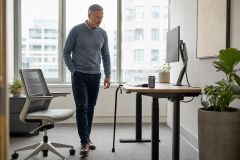 Middle-aged worker using a cane in an office, assessing readiness to return to work.