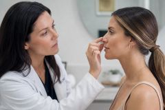 Cosmetic surgeon examining patient's nose in clinic consultation, assessing potential rhinoplasty refinement.
