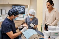 Pediatric dental exam in clinic: dentist and hygienist treating child while parent observes.