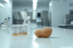 Close-up of a peanut next to laboratory vials in a modern, clean white science lab. Focus on food allergy research, testing, or analysis. Scientific environment, neutral colors, precise focus.