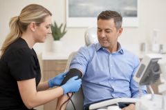 Dental clinic preoperative vitals check with clinician applying a blood pressure cuff to patient.