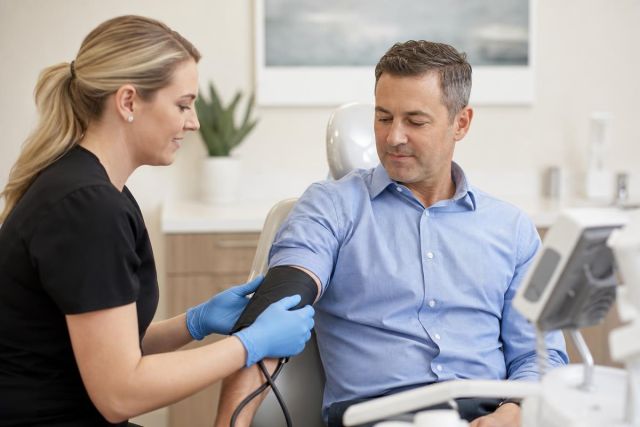 Dental clinic preoperative vitals check with clinician applying a blood pressure cuff to patient.