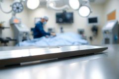 Surgical scene in an operating room. Medical equipment and a blurred surgeon in scrubs are visible. Sterile environment, bright lights, focus on a stainless steel surface.
